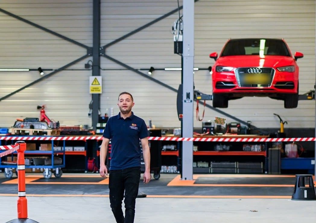 Tommy van Hooydonk, eigenaar van EV Refix, loopt door de werkhal aan de Kleine Krogt in Breda, met een auto op de brug achter hem.